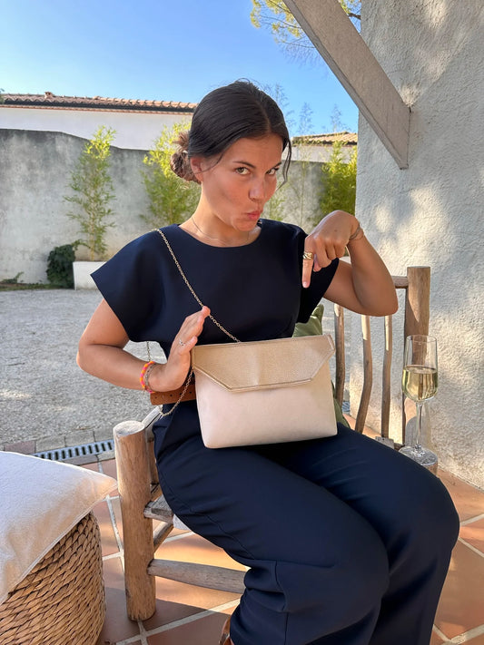 La pochette Isa zippée ivoire et dorée, portée sur les genoux.