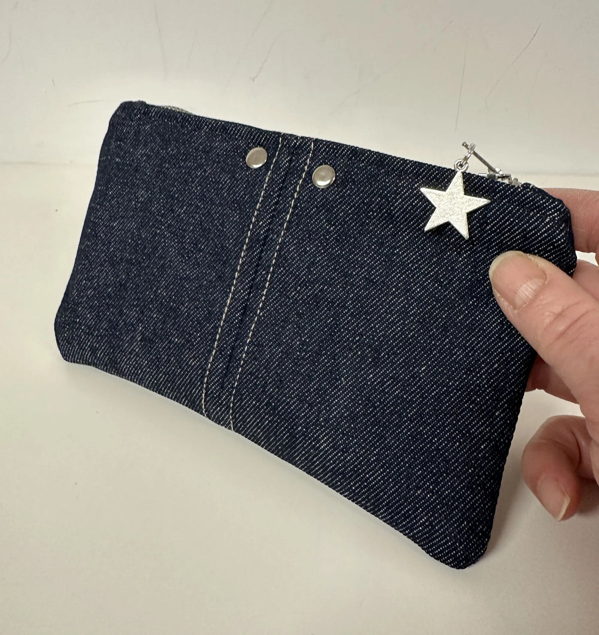 Le porte-monnaie en denim brut, tenu en main.