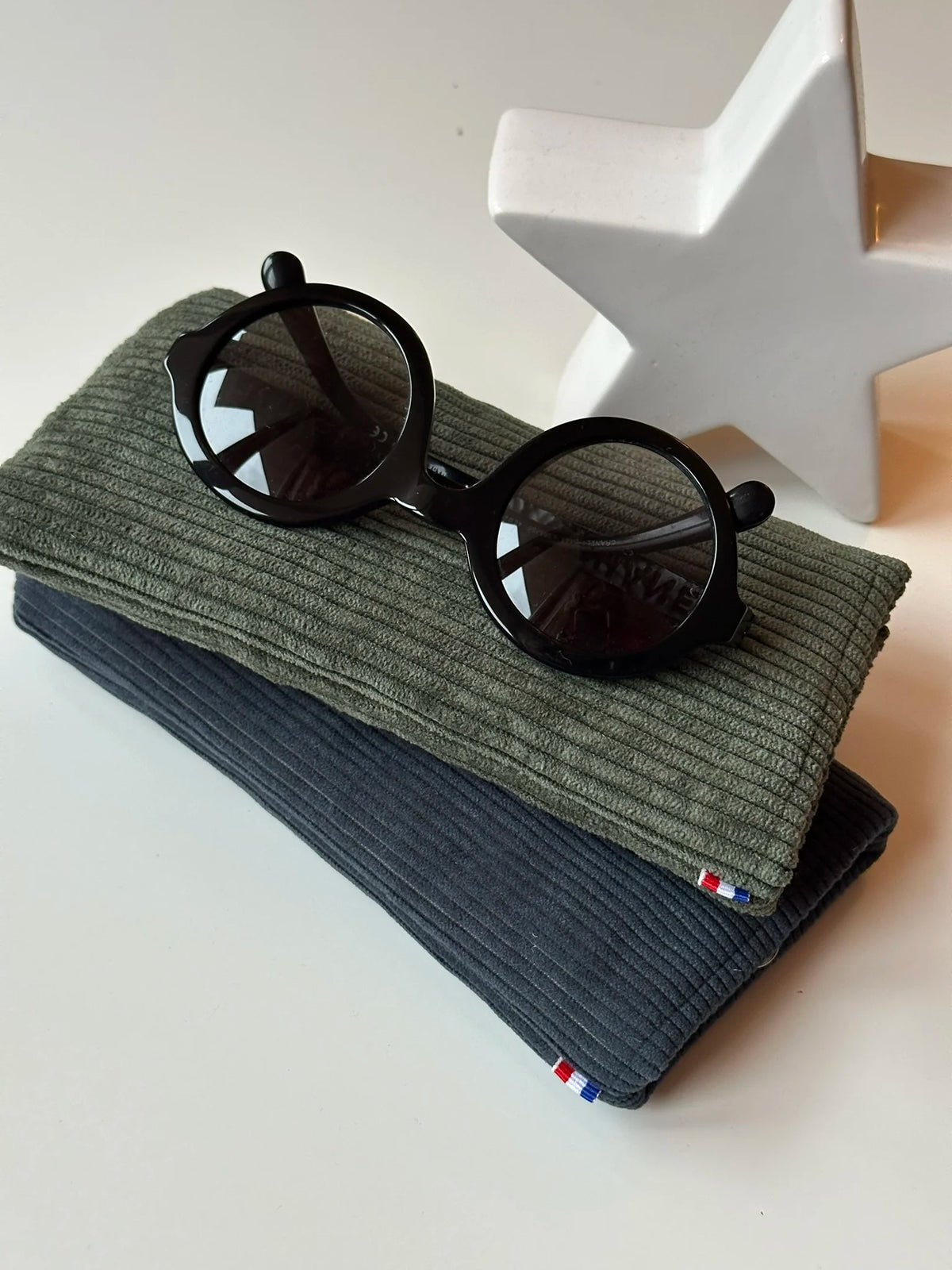 L'étui à lunettes en velours cotelé bleu canard sous le vert kaki.