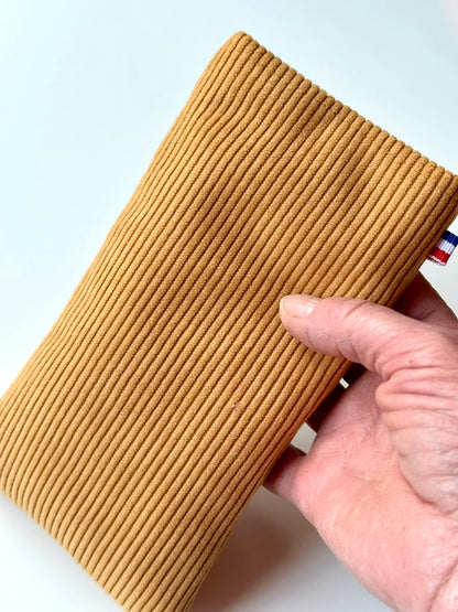 L'étui à lunettes en velours cotelé jaune moutarde, dans la main.