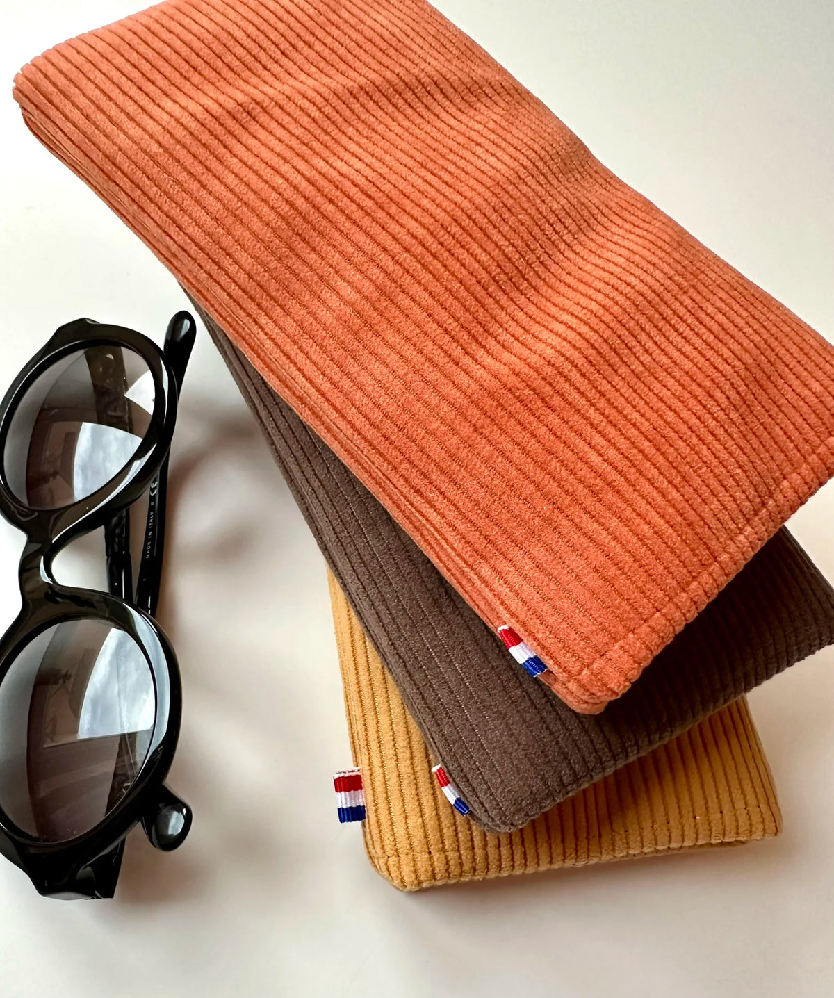 L'étui à lunettes en velours cotelé orange, posé sur le marron et le jaune moutarde.