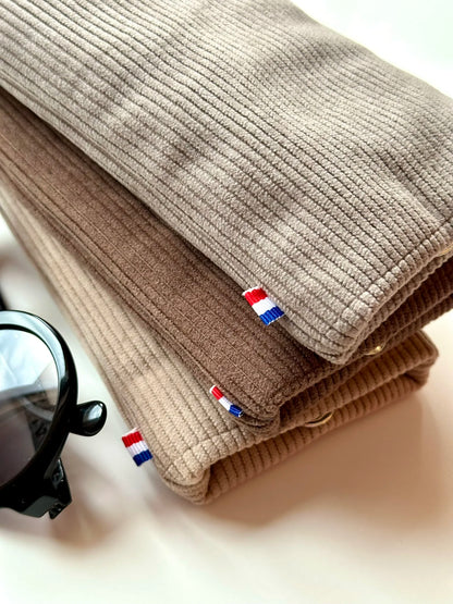 L'étui à lunettes en velours cotelé taupe, posé sur le marron chamois et le beige.