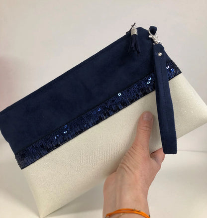 La pochette Isa zippée bleu marine et blanc à paillettes avec sa dragonne amovible, dans la main.