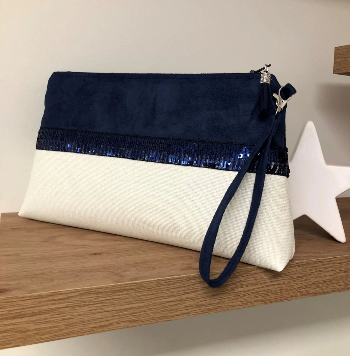La pochette Isa zippée bleu marine et blanc à paillettes avec sa dragonne amovible pour le poignet.