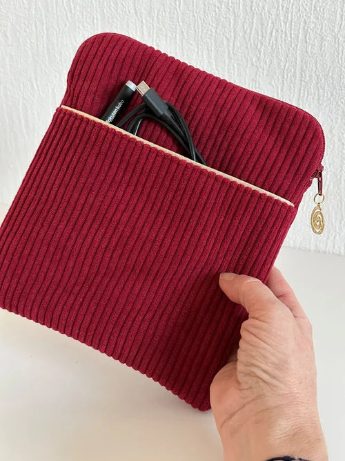 La pochette liseuse en velours cotelé bordeaux, avec stylet et cable dans la poche avant, tenue dans la main.
