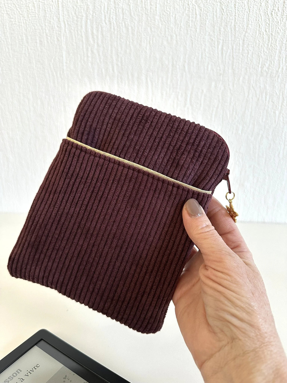 La pochette liseuse en velours prune, portée à la main, format 6 pouces.