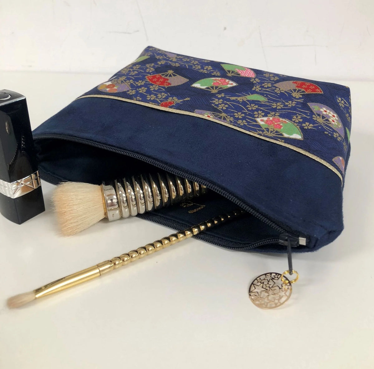 La pochette à maquillage bleu marine en tissu japonais Sakura éventails, garnie de cosmétiques.