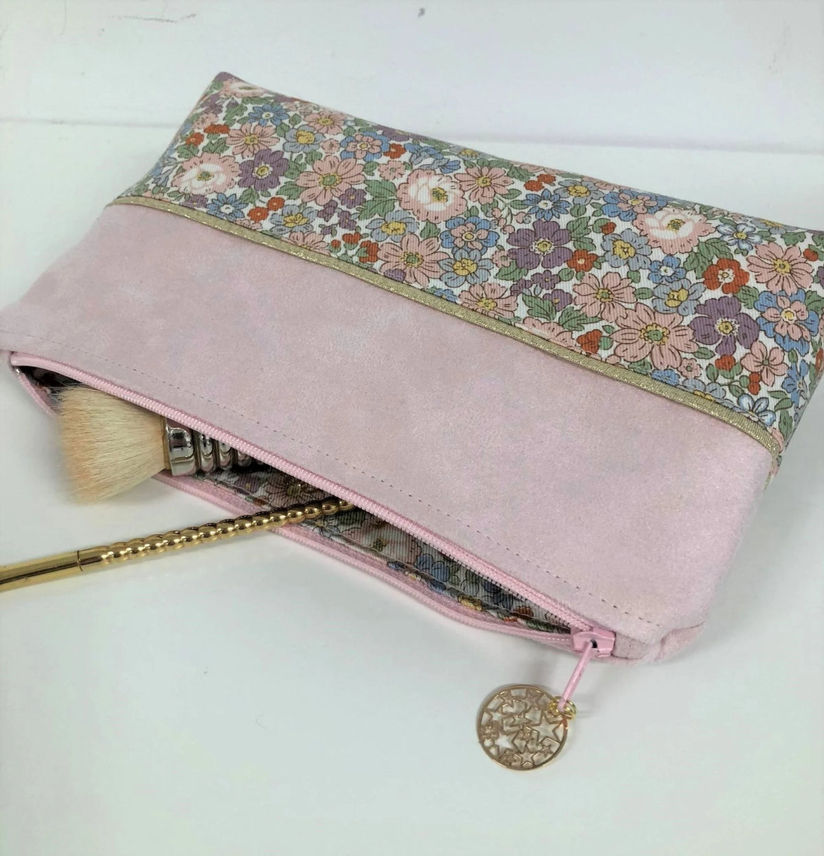 La pochette à maquillage rose et dorée à fleurs pastel, entrouverte.
