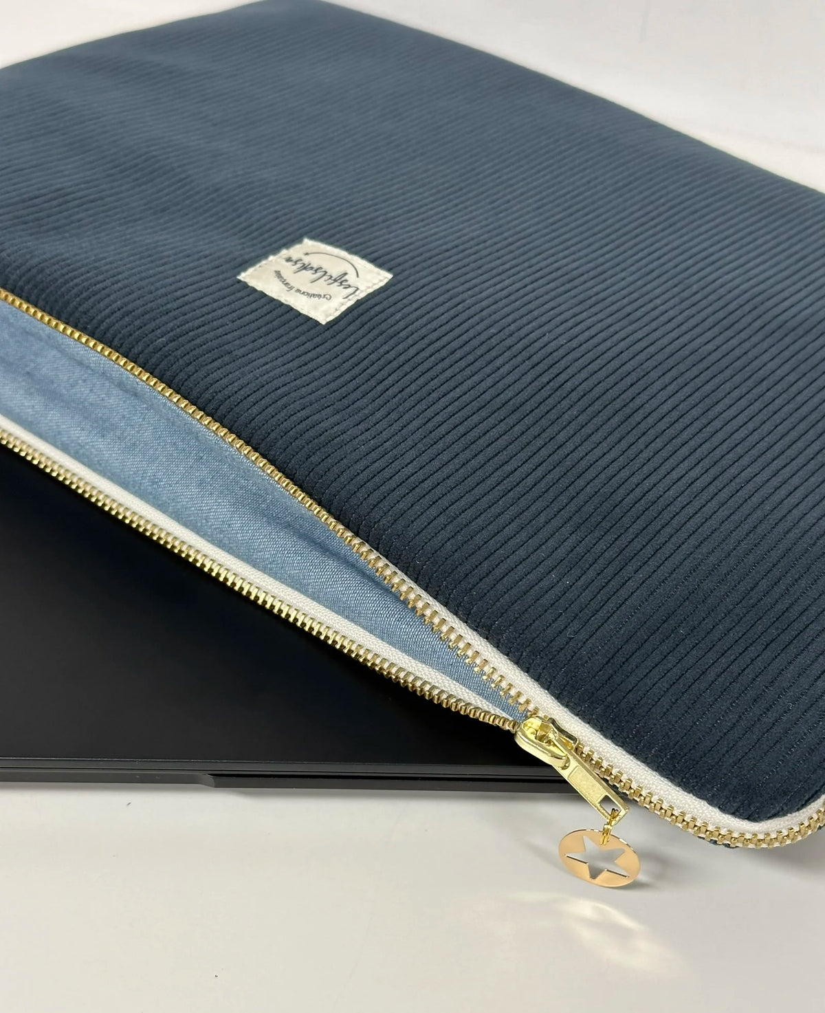 La pochette ordinateur en velours cotelé bleu canard, entrouverte.