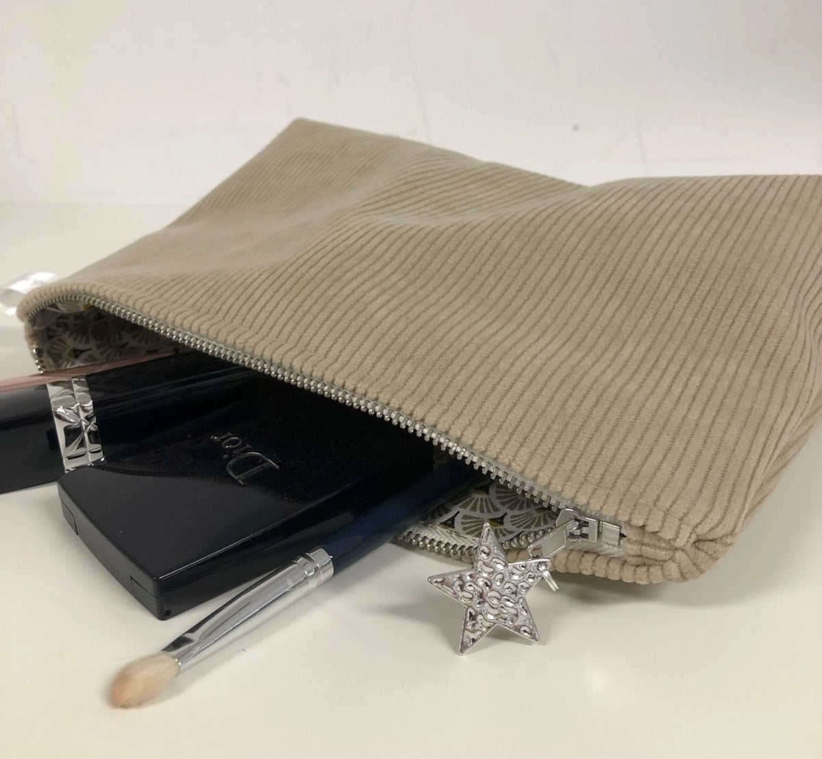 La pochette en velours côtelé beige sable, contenant du maquillage