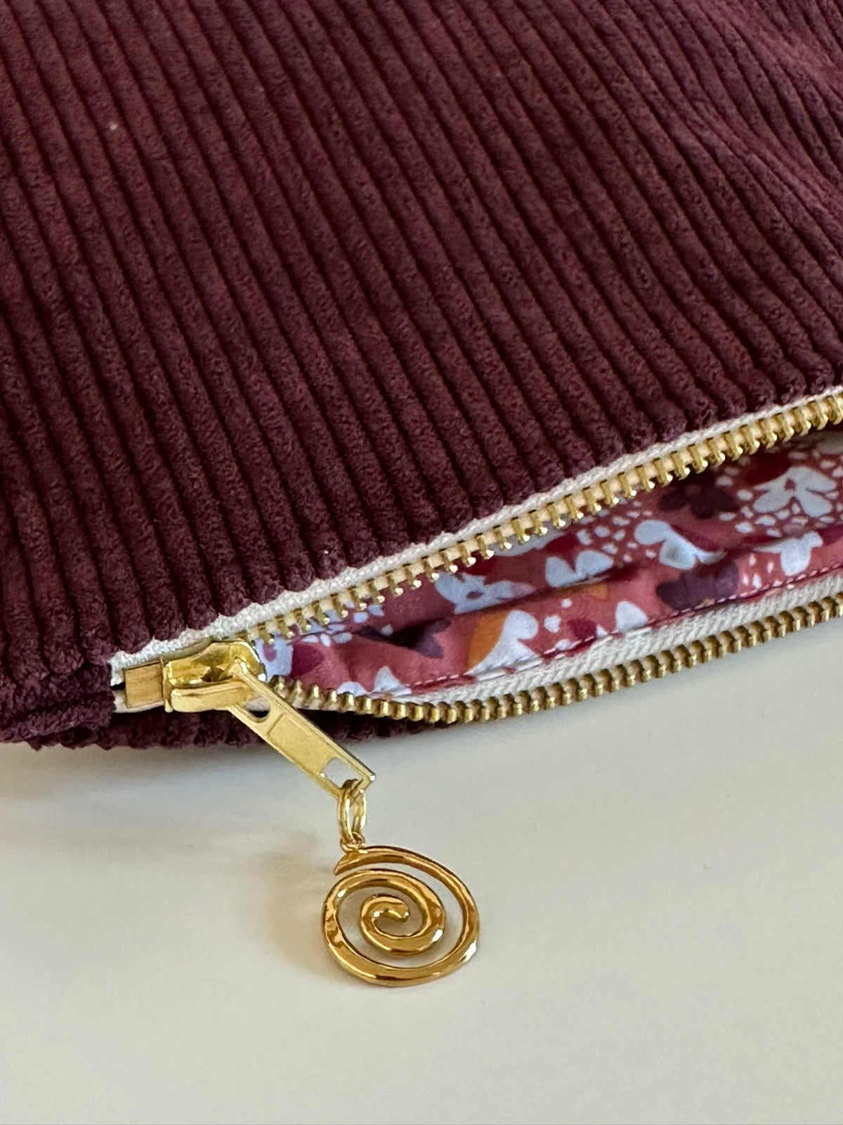 La fermeture zippée métal dorée de la pochette en velours côtelé prune.