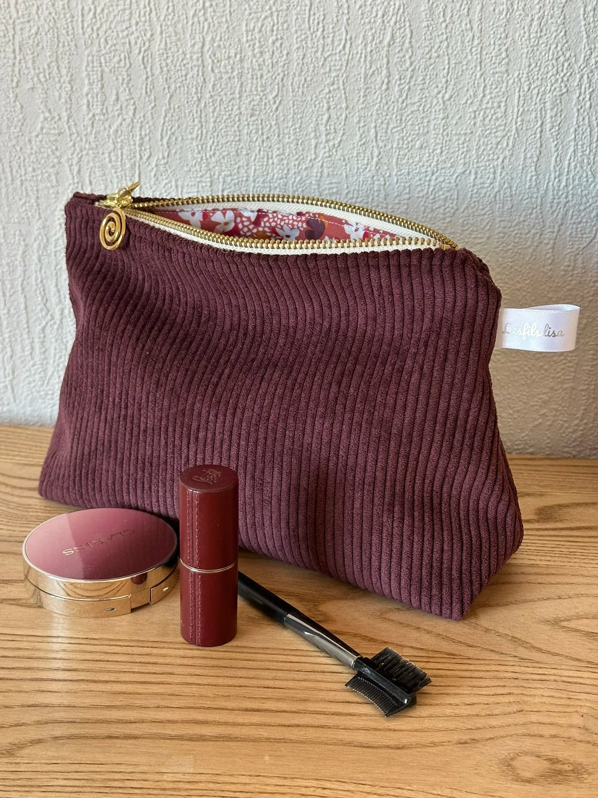 La pochette en velours côtelé prune, livré sans les accessoires maquillage présentés.