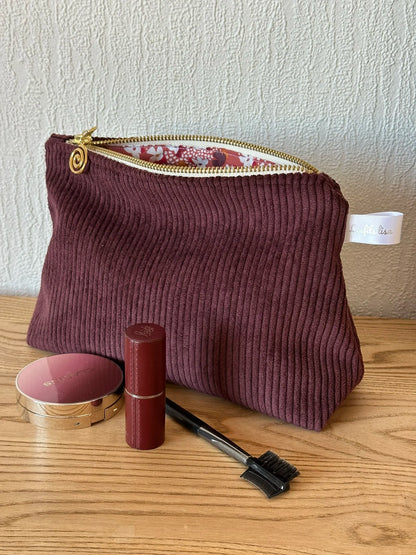 La pochette en velours côtelé prune, livré sans les accessoires maquillage présentés.