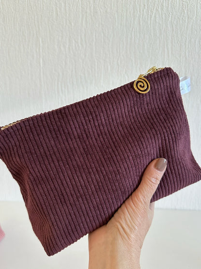 La pochette en velours côtelé prune, présentée en main.