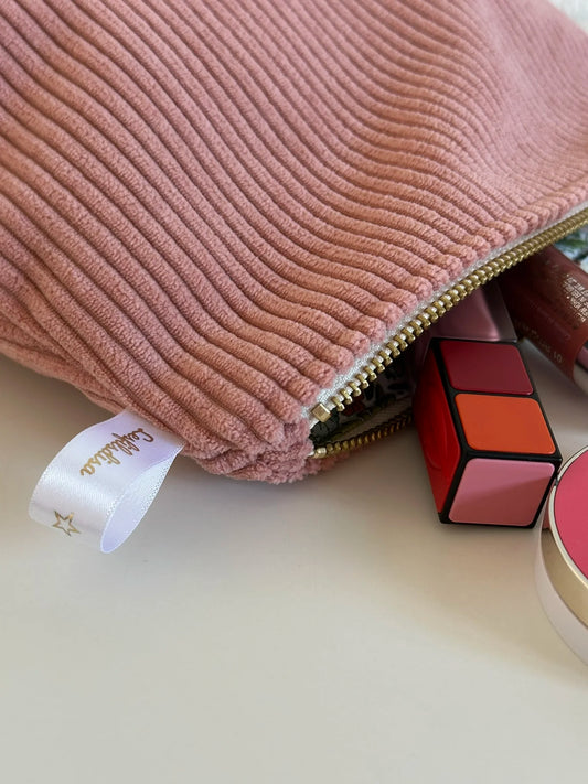 La fermeture éclair dorée de pochette en velours côtelé rose blush.