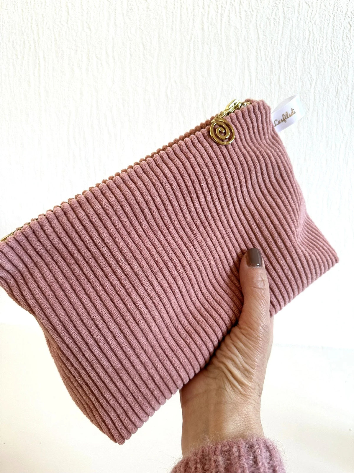 La pochette en velours côtelé rose blush portée en main.