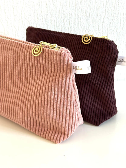 La pochette en velours côtelé rose blush devant la pochette prune.