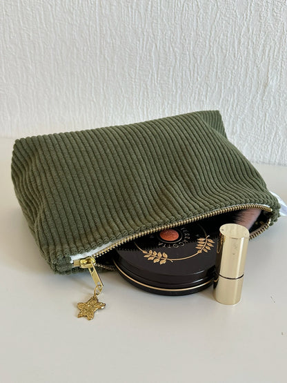 La pochette en velours côtelé vert armée, ouverte, avec accessoires de maquillage ( non fournis).