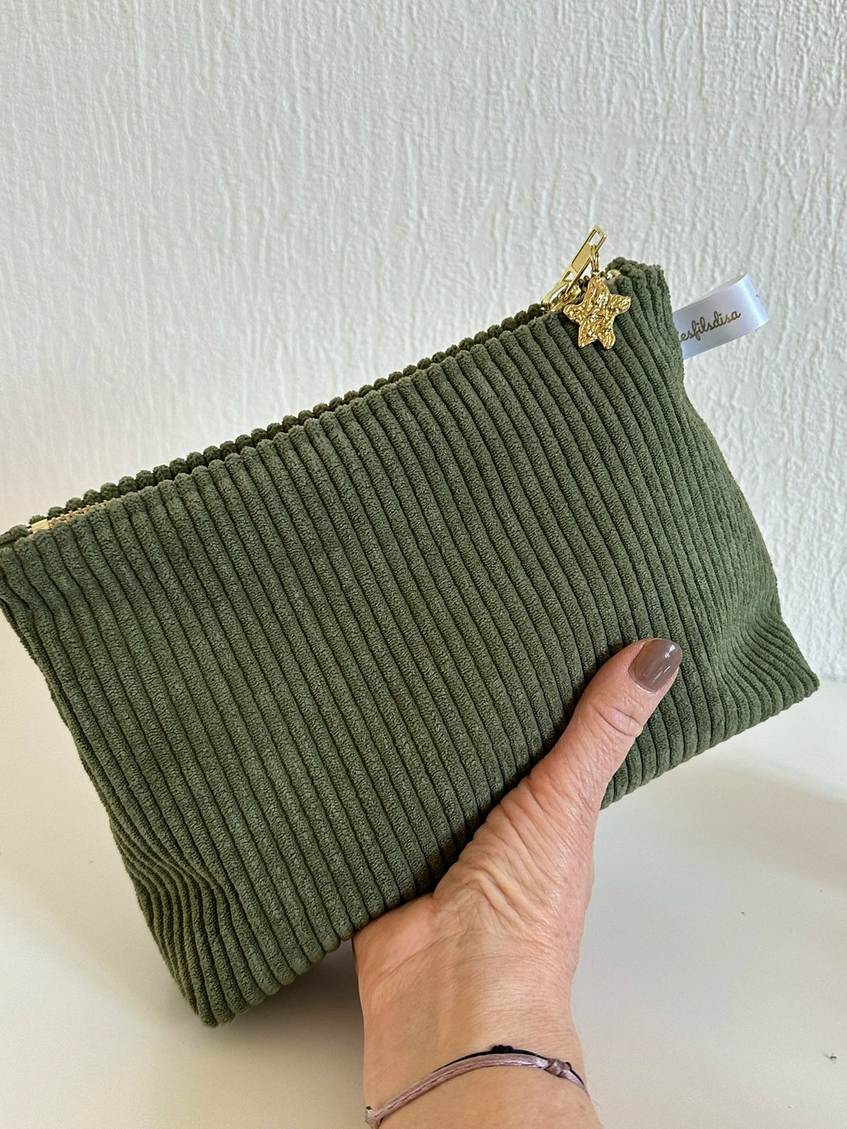 La pochette en velours côtelé vert armée, tenue dans la main.