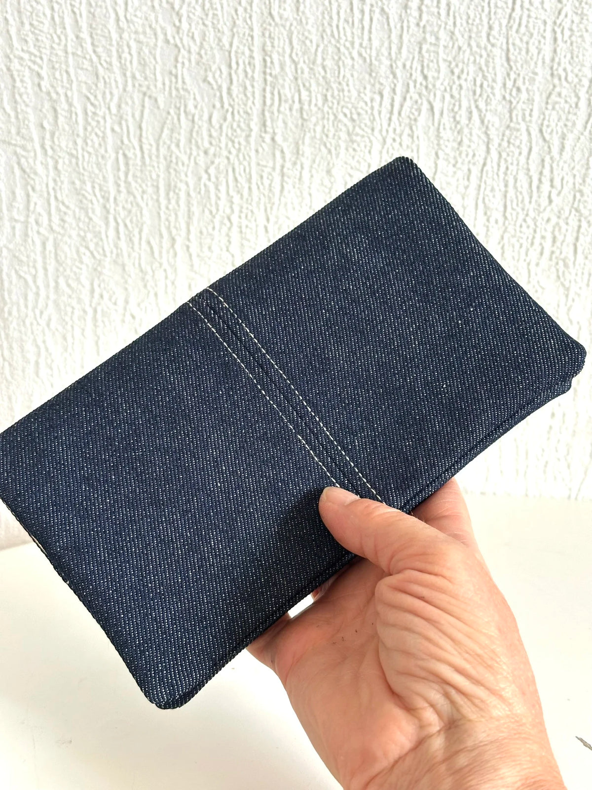 Le porte chéquier en denim tenu en main.