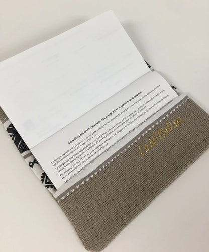 Le rabat inférieur du porte-chéquier ethnique beige, blanc et doré.