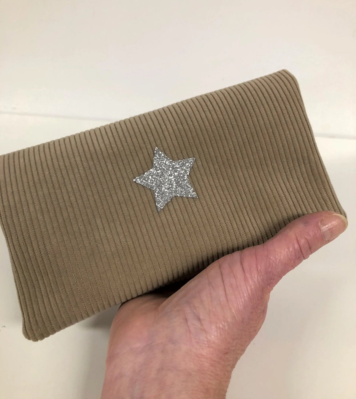 Le porte chéquier en velours tricoté beige avec étoile pailletée argentée, tenu en main.