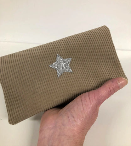 Le porte chéquier en velours tricoté beige avec étoile pailletée argentée, tenu en main.