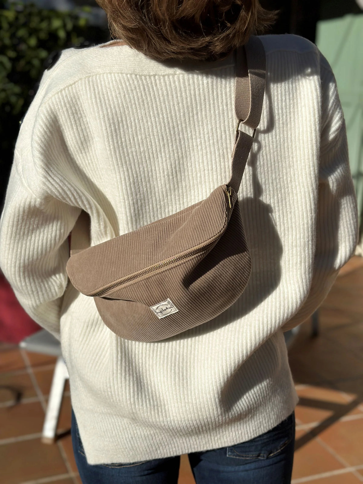 Le sac banane en velours côtelé beige, porté en travers.