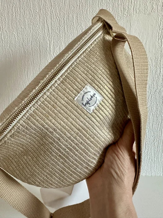 Le sac banane en velours cotelé doré, tenu à la main