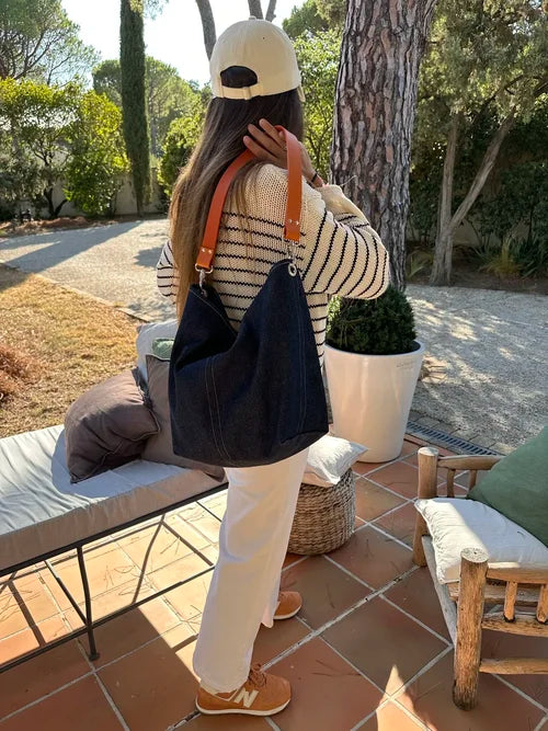 Vue d'ensemble du sac hobo en denim et son anse en cuir orange posé sur l'épaule.