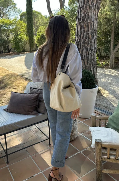 Le sac Hobo en lin ivoire et anse amovible en cuir bleu, porté à l'épaule.