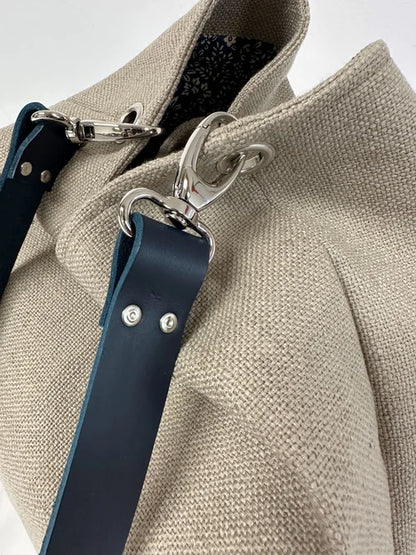 Les mousquetons d'accroche sur le sac Hobo en lin beige et son anse en cuir bleu marine 