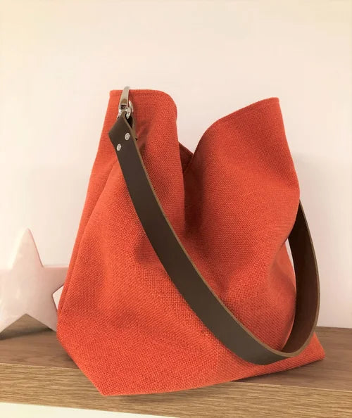 Le sac Hobo en lin orangé et son anse en cuir marron amovible.
