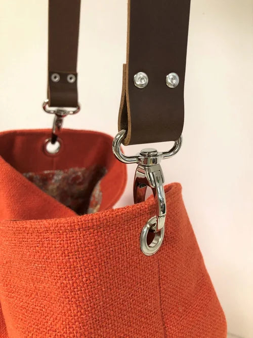 Les mousquetons d'accroche de l'anse en cuir du sac Hobo en lin orangé et son anse en cuir marron amovible