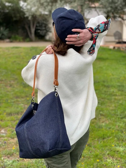 Le sac hobo en toile denim brut et son anse en cuir fauve porté à l'épaule