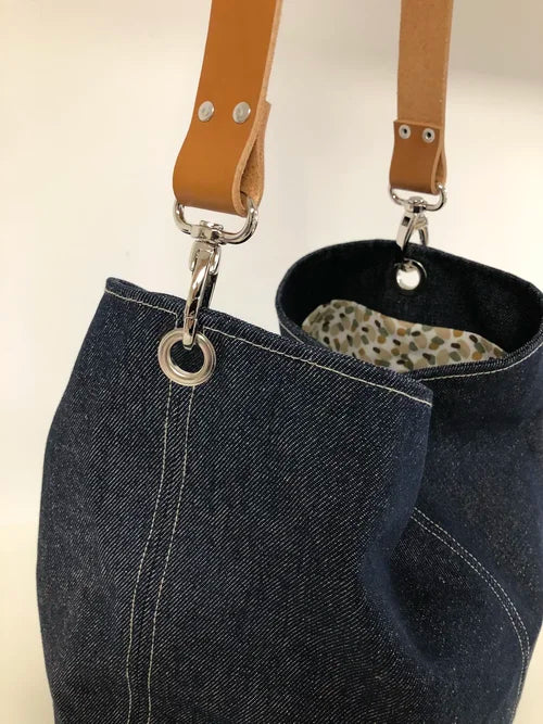 Vue détaillée des accroches du sac hobo en toile denim brut et son anse en cuir fauve