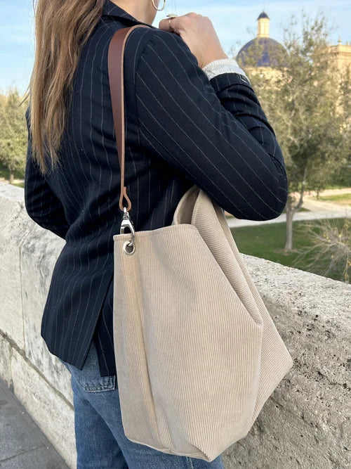 Le sac hobo en velours cotelé beige et son anse en cuir marron, porté à l'épaule par jeune femme