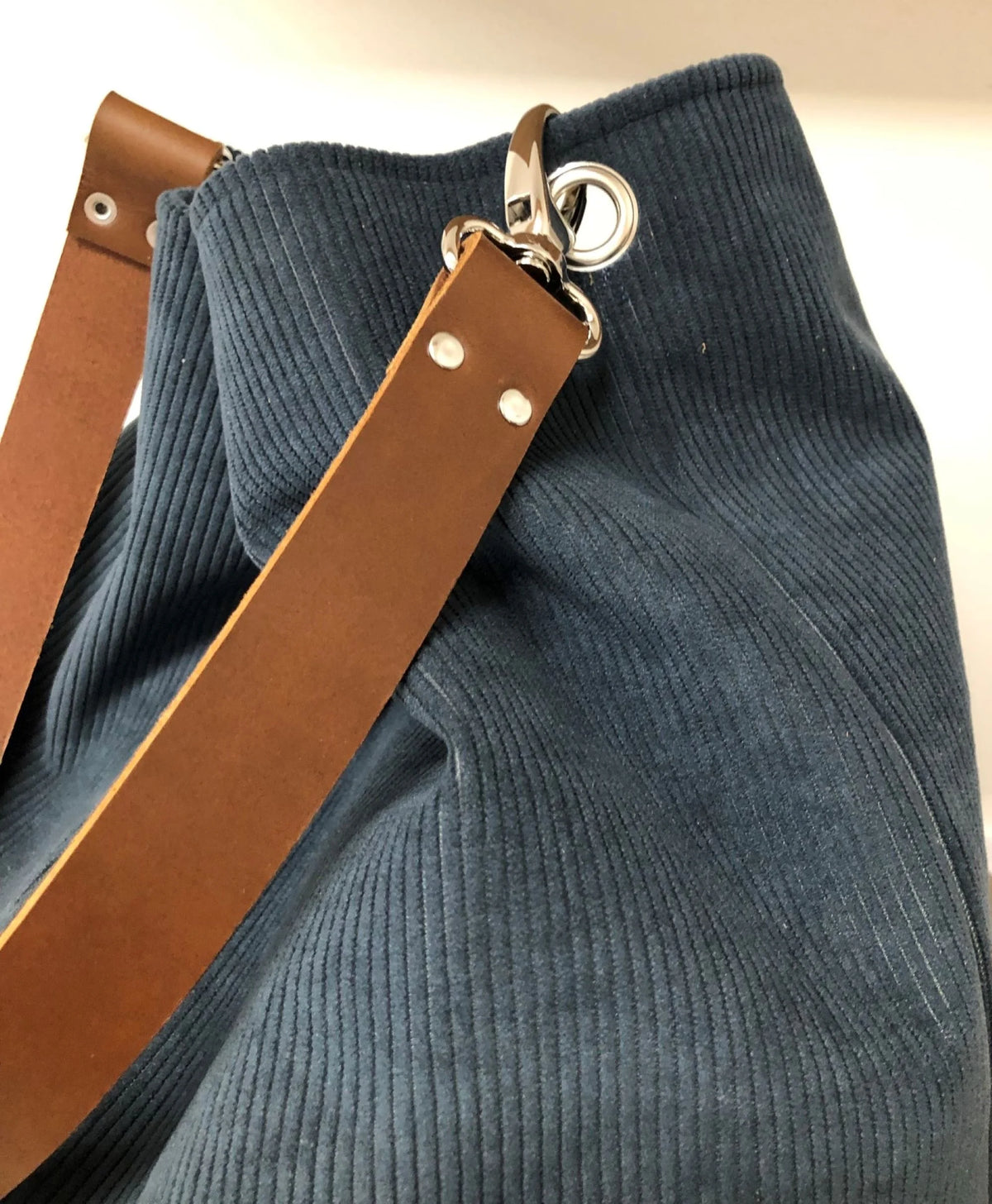 Vue détaillée de l'anse en cuir amovible du sac hobo en velours cotelé bleu canard.