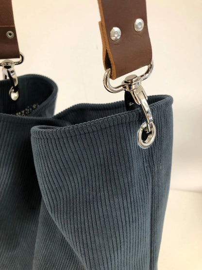 Les mousquetons de l'anse en cuir du sac hobo en velours cotelé bleu canard.