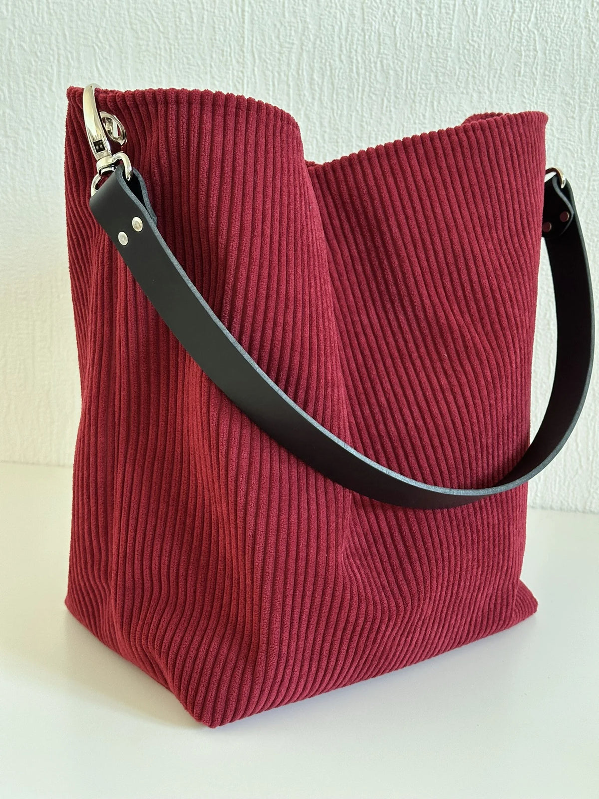 Vue d'ensemble du sac Hobo en velours cotelé bordeaux, et anse en cuir noir.