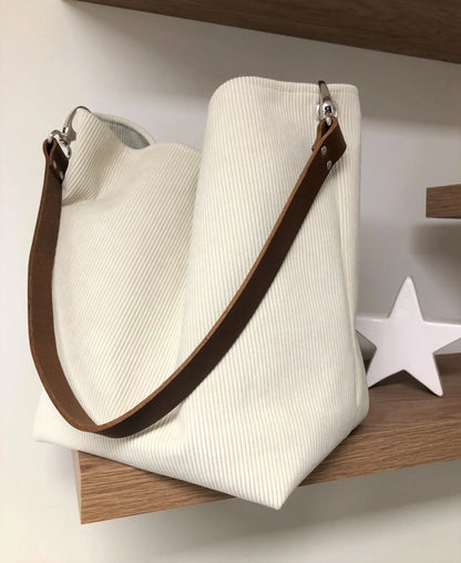 Le sac hobo en velours cotelé ivoire et son anse en cuir marron.