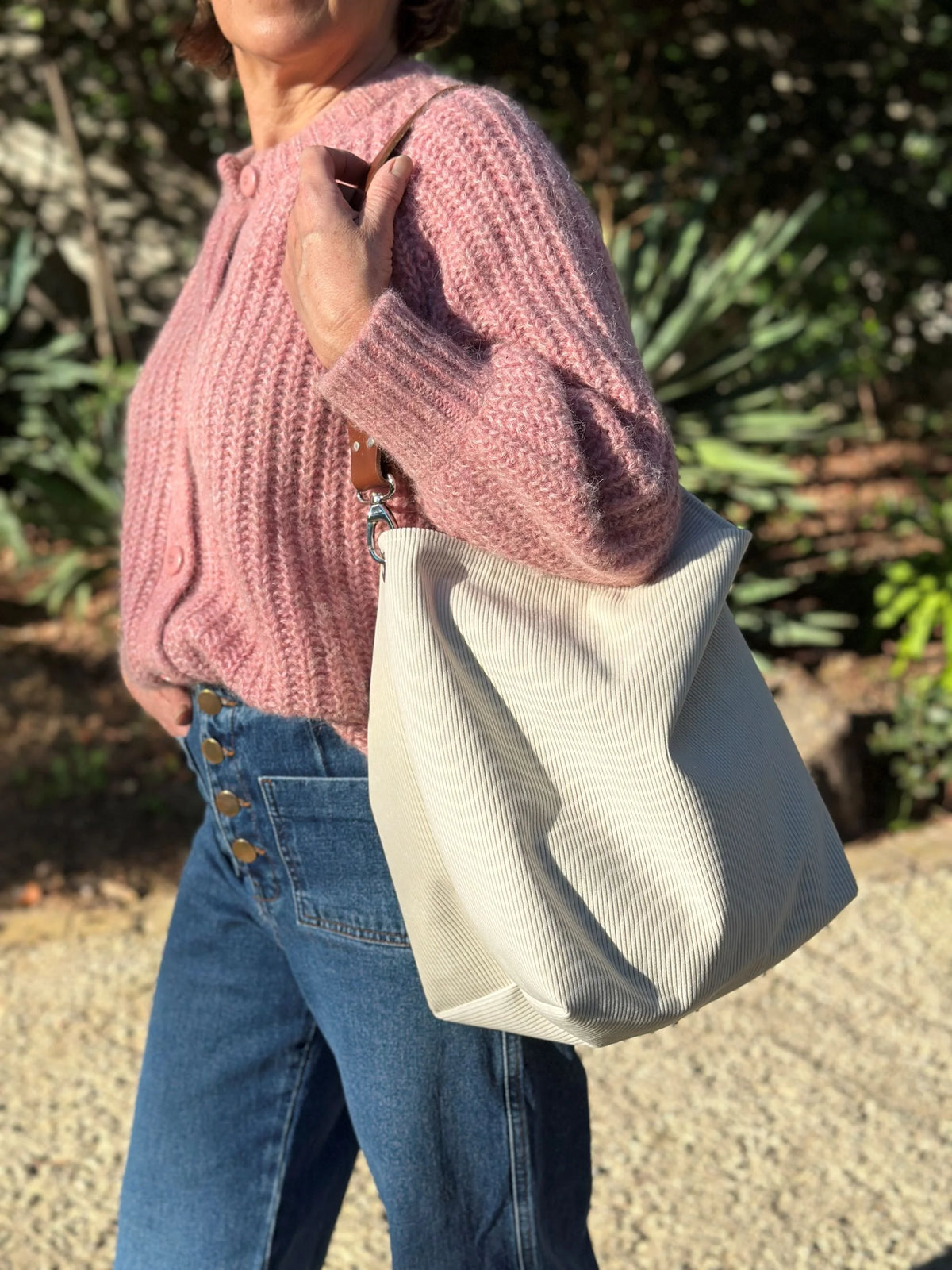 Femme portant le sac hobo en velours cotelé ivoire et son anse en cuir fauve.