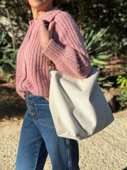 Femme portant le sac hobo en velours cotelé ivoire et son anse en cuir fauve.