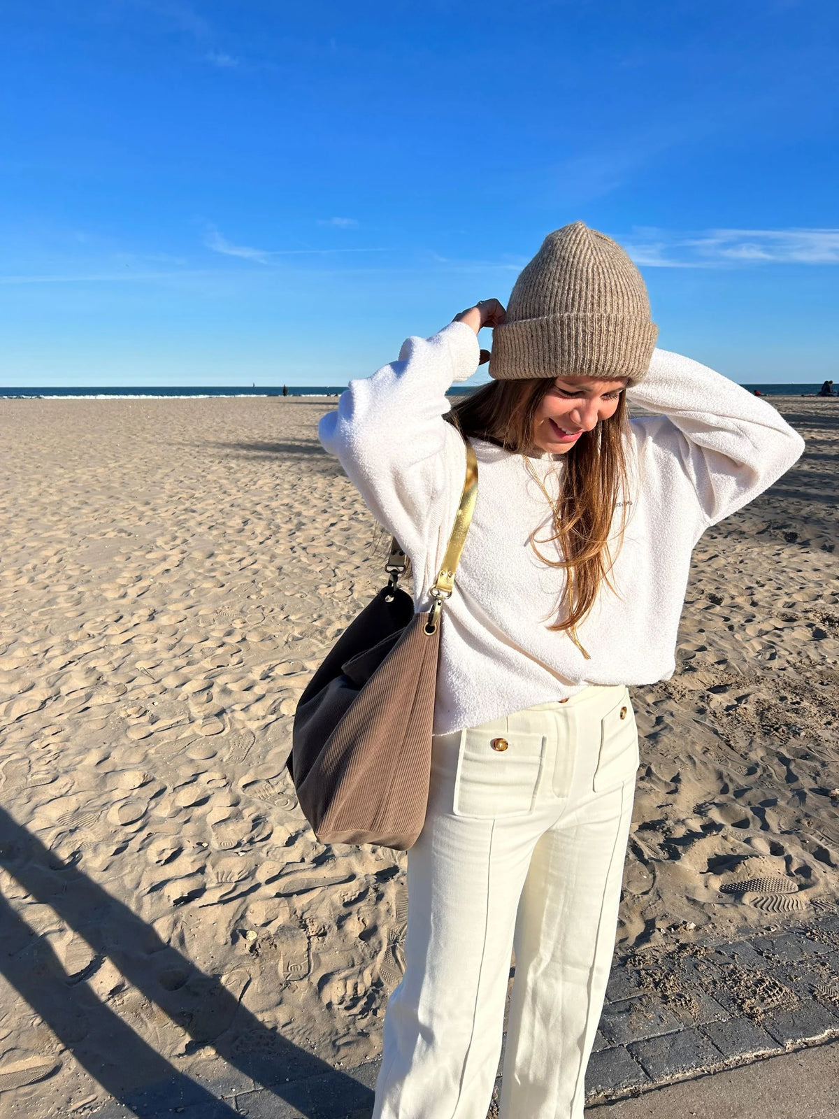 Le sac hobo en velours cotelé marron chamois et son anse en cuir doré, porté à l'épaule.