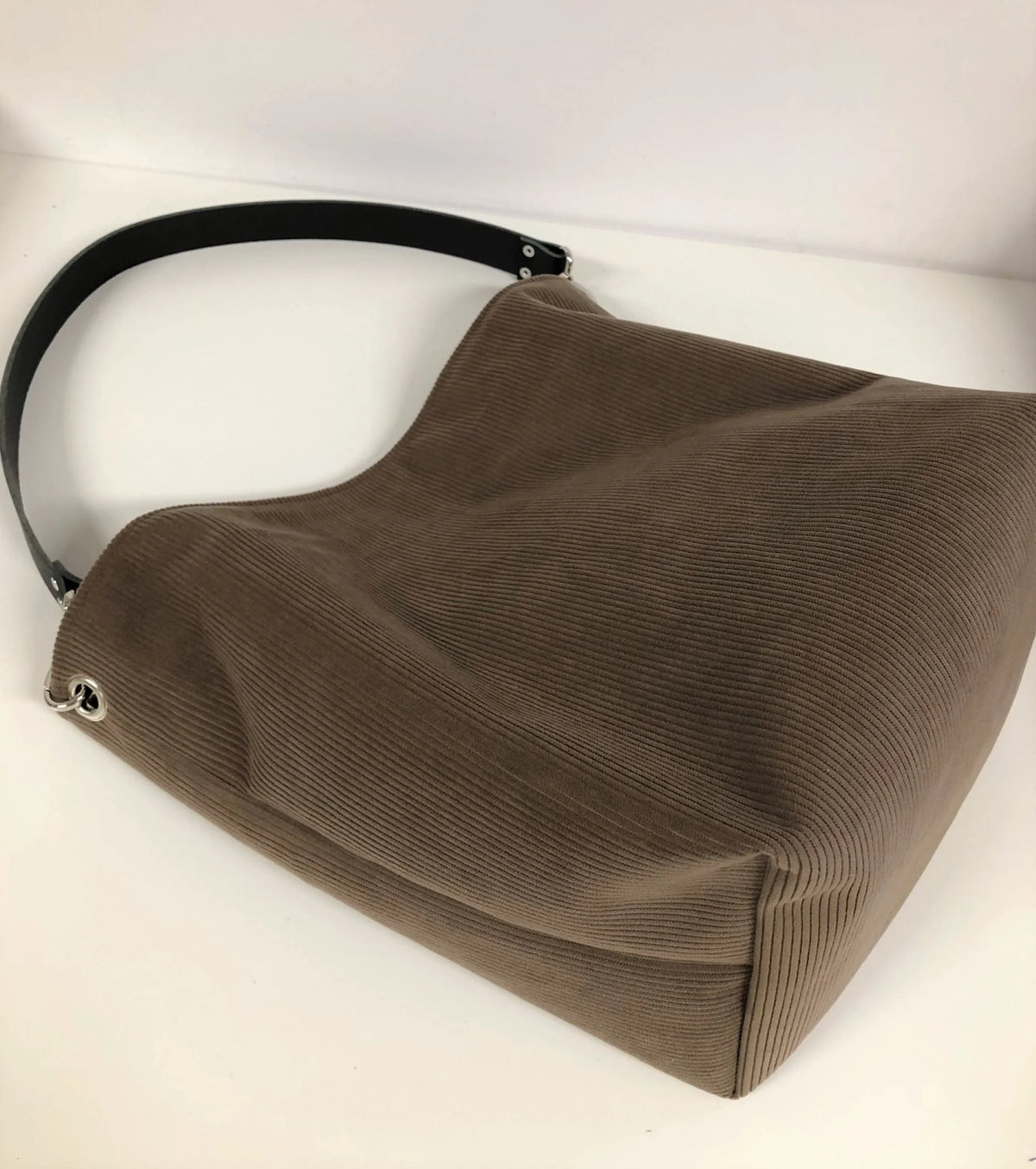 Le fond du sac hobo en velours cotelé marron chamois et son anse en cuir noir.