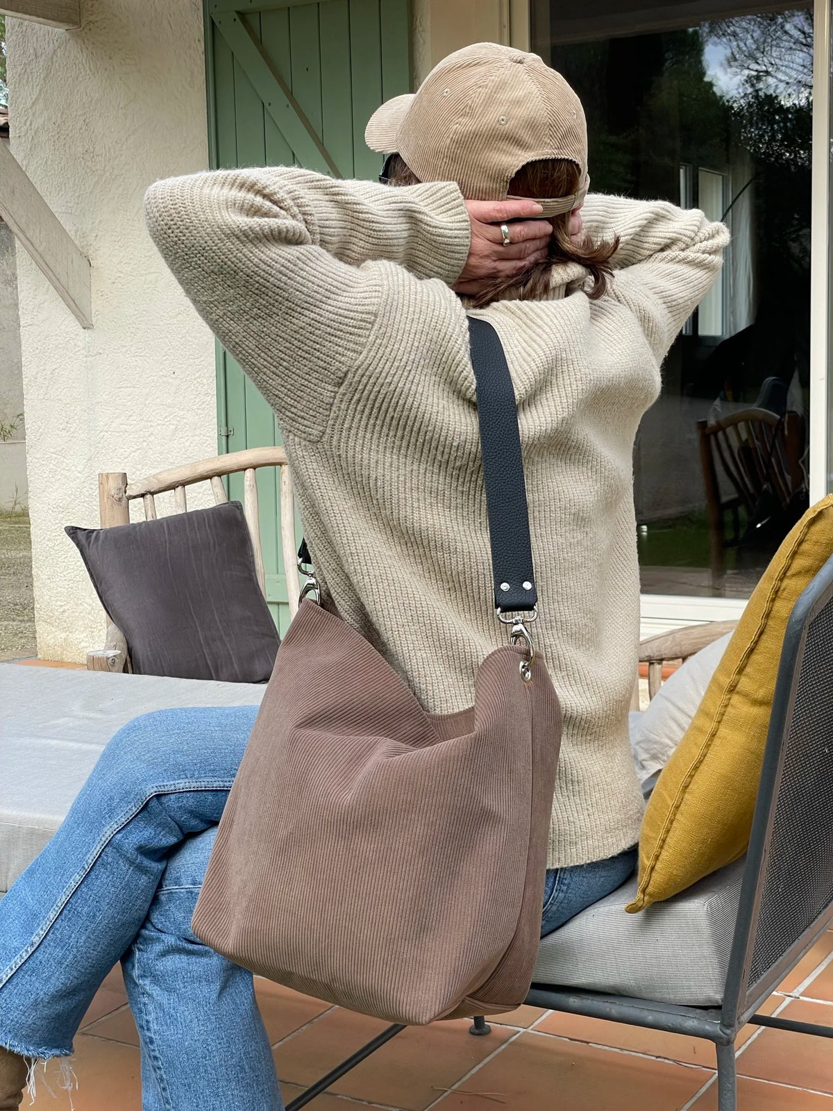 Le sac hobo en velours cotelé marron chamois et son anse en cuir noir, porté à l'épaule.