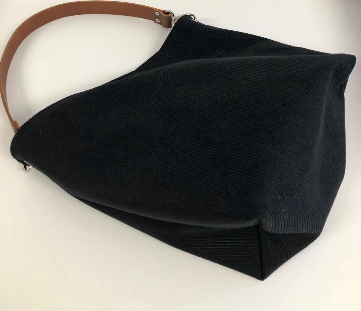 Le fond du sac hobo en velours cotelé noir et son anse en cuir marron.