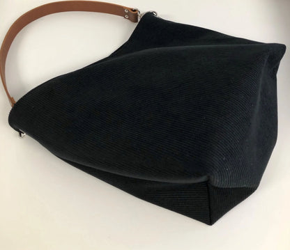 Le fond du sac hobo en velours cotelé noir et son anse en cuir marron.