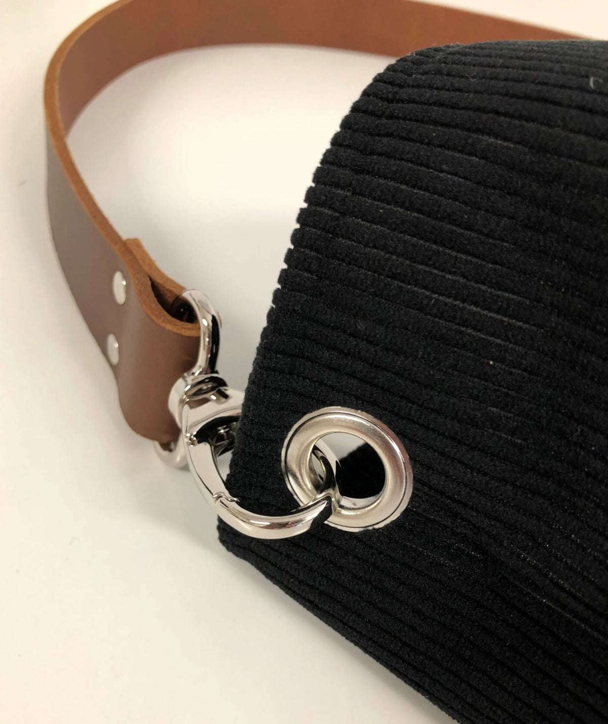 Vue détaillée de l'anse en cuir amovible du sac hobo en velours cotelé noir et son anse en cuir marron.