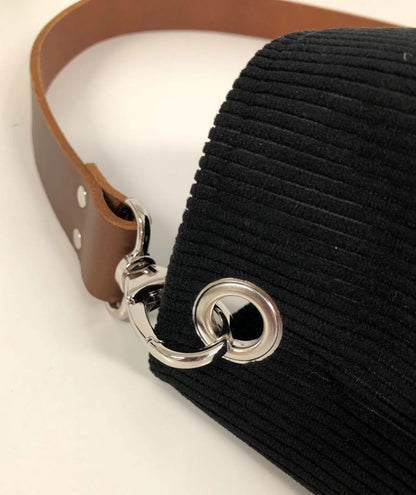 Vue détaillée de l'anse en cuir amovible du sac hobo en velours cotelé noir et son anse en cuir marron.